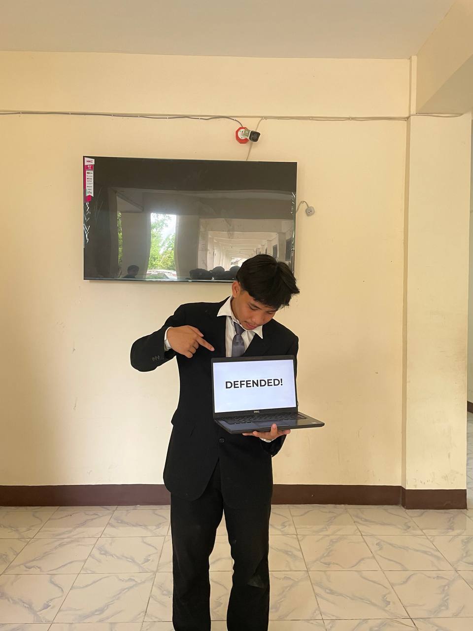 Von holding a laptop displaying the word Defended after the capstone presentation